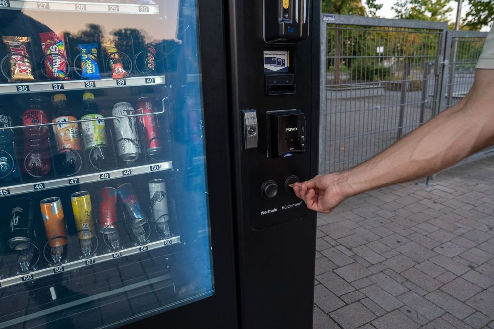 Hand wirft eine Münze in den Münzeinwurf eines Pulse Snackautomaten